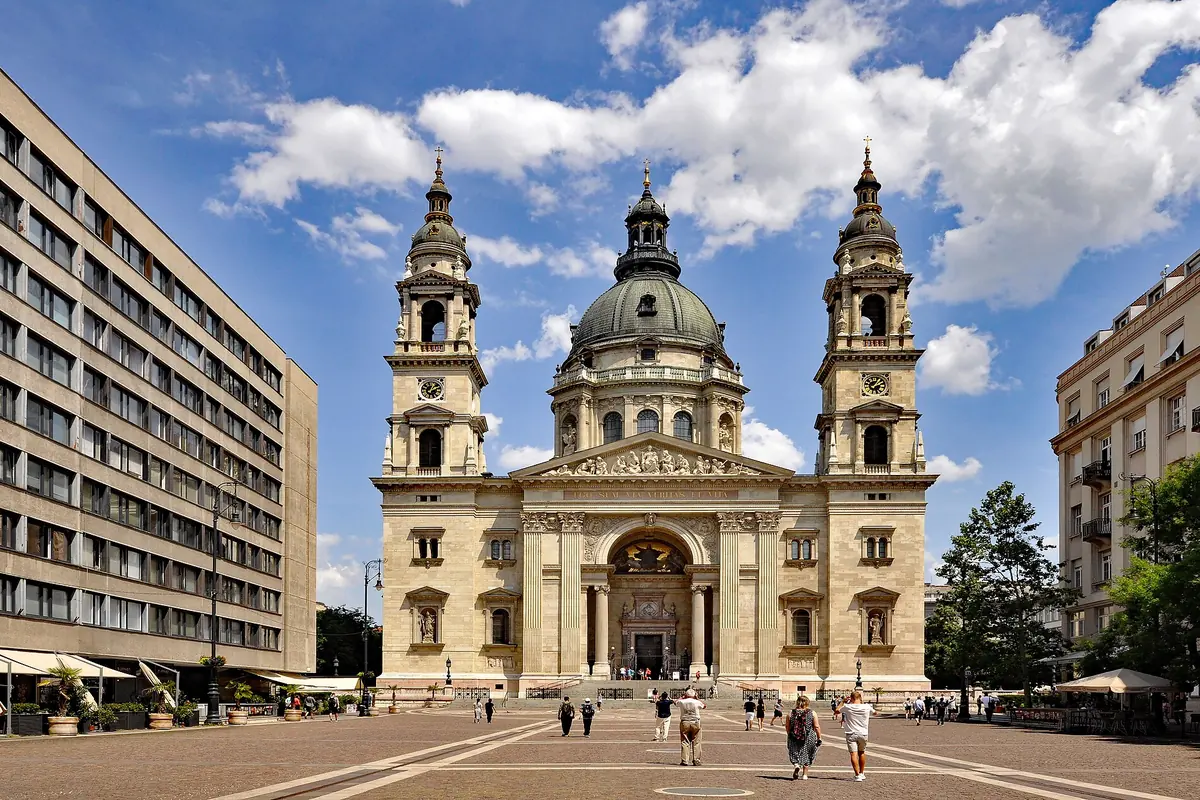 The west front of the basilica with two bell towers, a central dome and a portico, seen across a paved square.