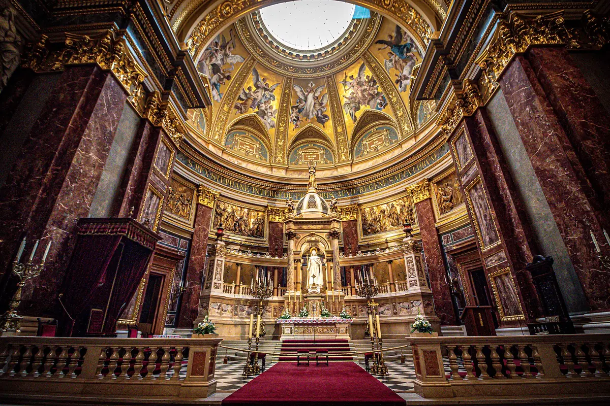 The nave and sanctuary of St Stephen's Basilica with a red carpet, marble columns and a dome with a skylight overhead.